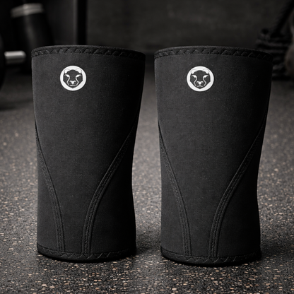 Pair of Mammal Strength Stiff Knee Sleeves PRO shown on a gym floor, featuring ultra-stiff black 7mm CR neoprene and PRO branding
